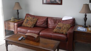 A living room with a brown leather sofa, two lamps, a painting, and a wooden coffee table. - Sugar Ski & Country Club Unit 11-803 Silver (Banner Elk)