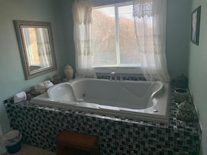A bathroom with a large bathtub, a mirror, and a window with curtains.