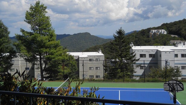 A tennis court with a blue surface, surrounded by trees and buildings. - Sugar Ski & Country Club Unit 113 Bronze (Banner Elk)