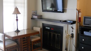 A living room with a fireplace, a television mounted above it, a table with chairs, and a lamp. - Sugar Ski & Country Club Unit 113 Bronze (Banner Elk)