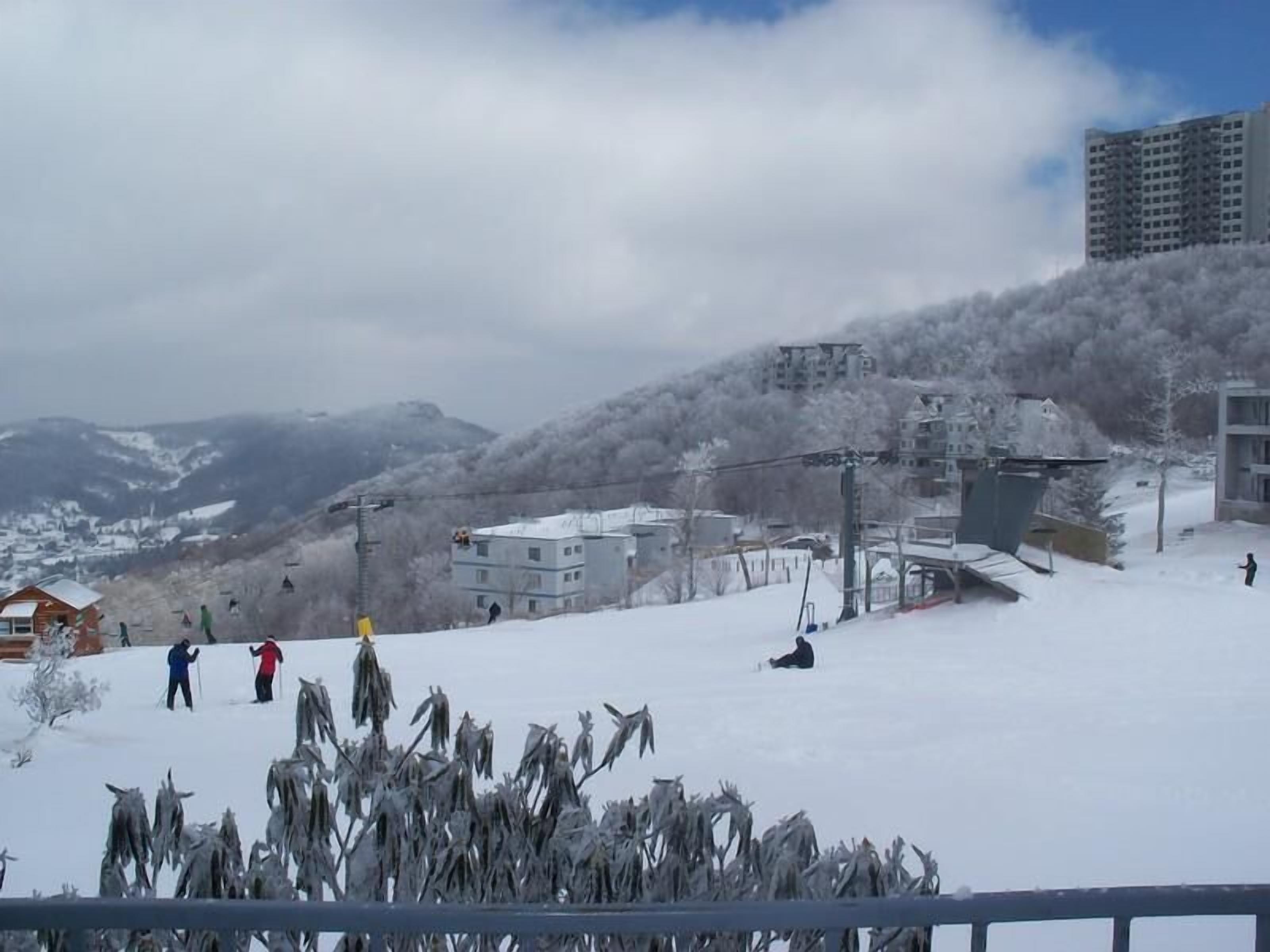 A snowy mountain landscape with a ski lift, buildings, and a person skiing.