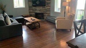 Ein Wohnzimmer mit Kamin aus Stein, einem flachbildfernseher darüber, einer Couch, einem Couchtisch und einem Sessel.