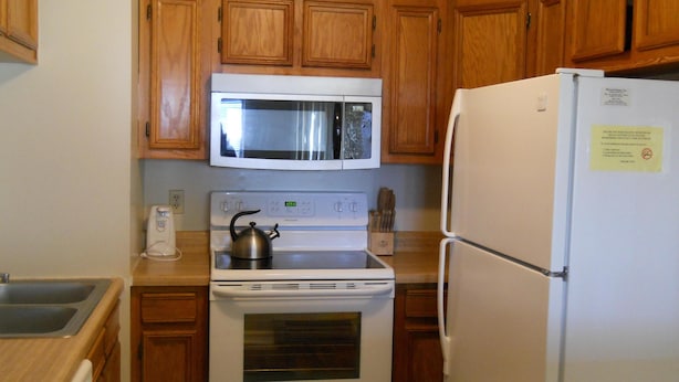 A kitchen with wooden cabinets, a white stove, a microwave, and a refrigerator. - Sugar Ski & Country Club Unit 413 Silver (Banner Elk)