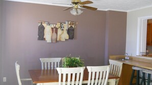 A dining area with a wooden table and white chairs, a ceiling fan, and a kitchen area with a bar counter. - Sugar Ski & Country Club Unit 413 Silver (Banner Elk)
