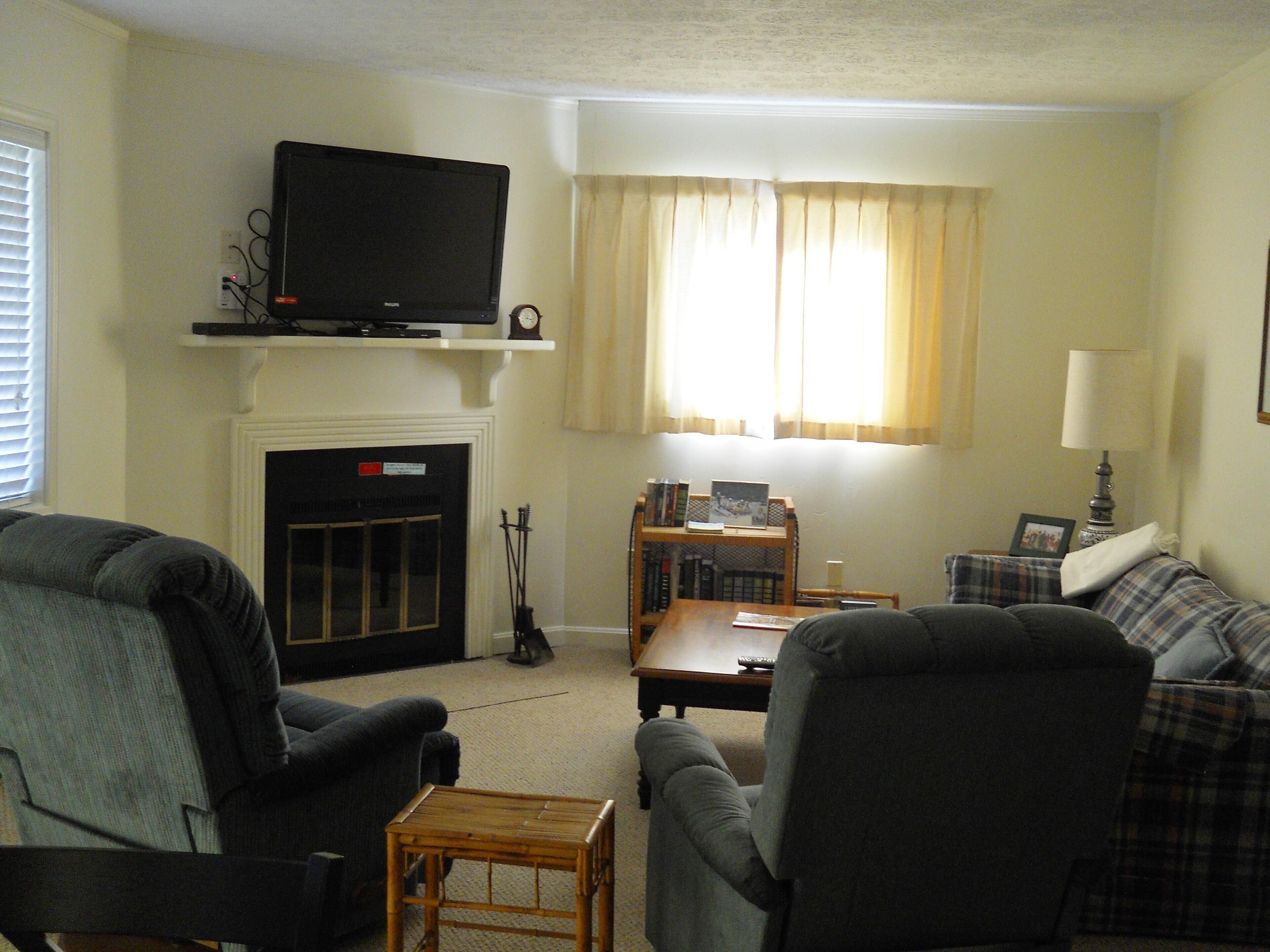 A living room with a fireplace, a television on a shelf, a sofa, a coffee table, and a lamp.