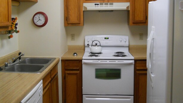 A kitchen with wooden cabinets, a white stove, a refrigerator, a sink, and a clock on the wall. - Sugar Ski & Country Club Unit 421 Bronze (Banner Elk)