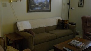 A living room with a sofa, a coffee table with magazines and a remote control, a lamp, and a painting on the wall. - Sugar Ski & Country Club Unit 421 Bronze (Banner Elk)