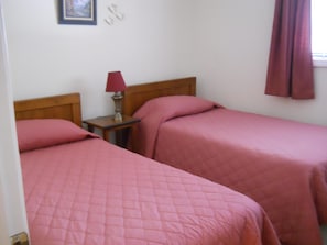 Ein Zimmer mit zwei Betten, jeweils mit einer rosa gesteppten Bettdecke, einem Holz-Kopfteil und einem Nachttisch mit Lampe.