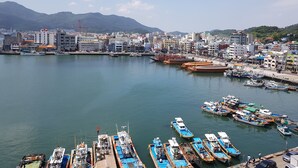 A harbor with boats docked, a cityscape in the background, and mountains. - Hotel Napoli (Tongyeong)