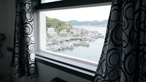 A window view of a marina with boats, buildings, and hills in the background. - Hotel Napoli (Tongyeong)