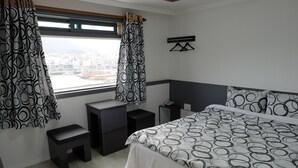 A modern hotel room with a large bed, a small desk, a nightstand, and a window with curtains. - Hotel Napoli (Tongyeong)