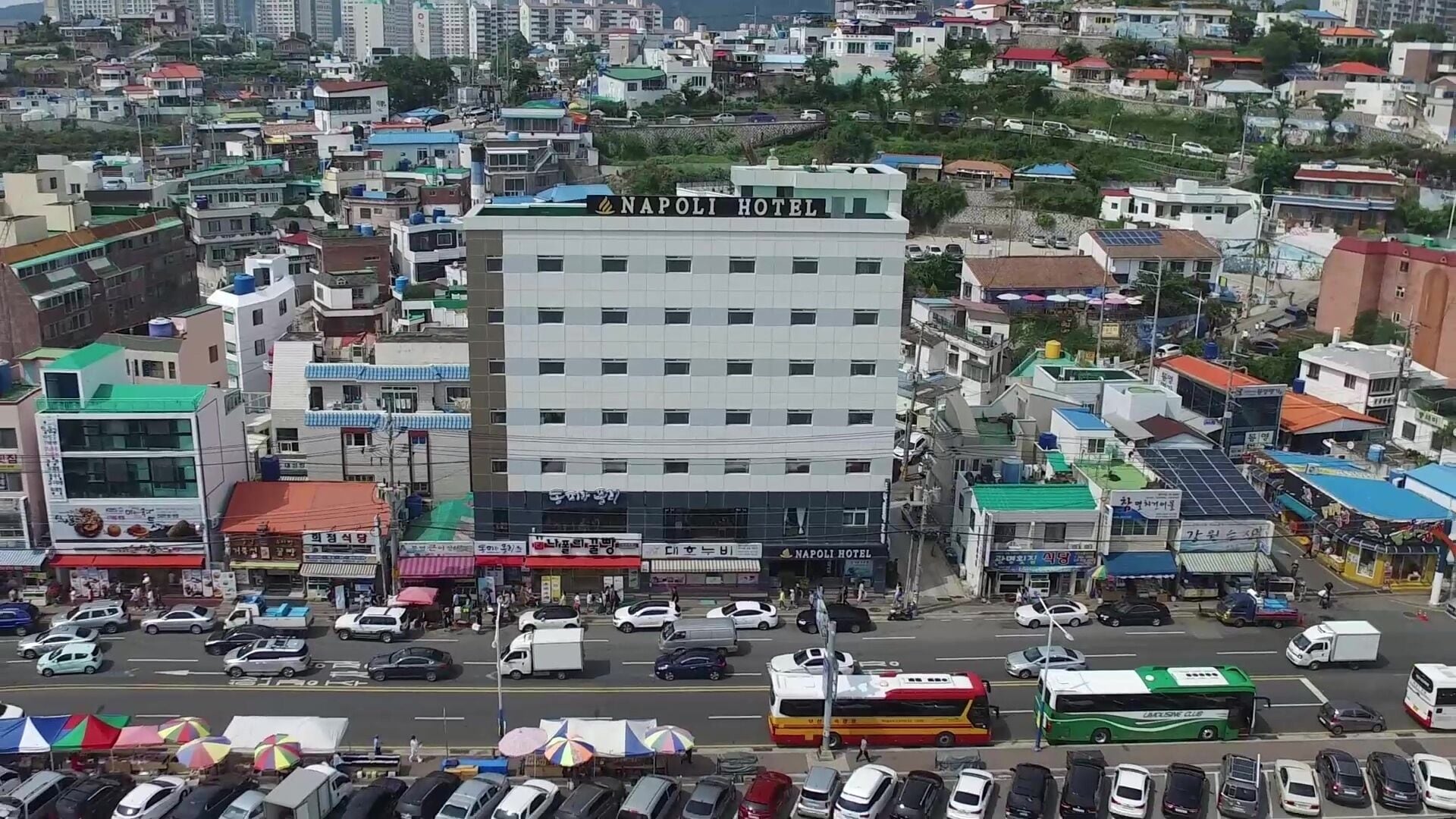 A multi-story hotel with a prominent sign, surrounded by a busy urban street with various vehicles and shops.
