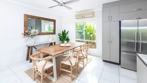 Cozinha moderna com área de jantar, incluindo mesa de madeira, cadeiras, ventilador de teto e geladeira.