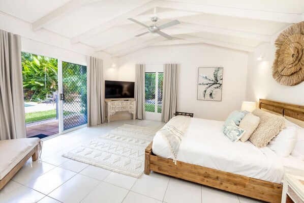 A bedroom with a bed, a TV, a ceiling fan, and a view of the outdoors.