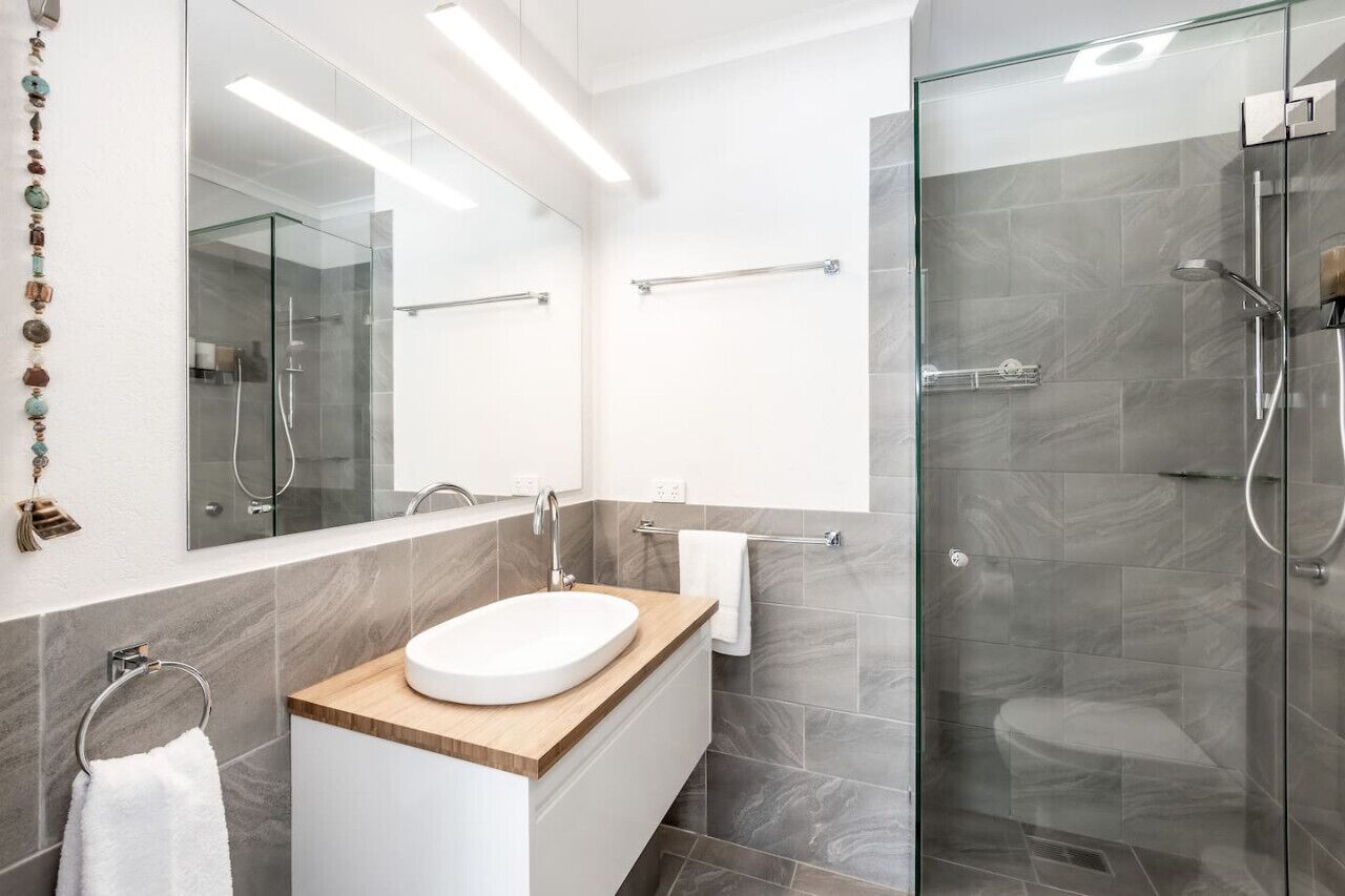 Une salle de bain moderne avec une douche à parois de verre, un lavabo blanc doté d’un plan de toilette en bois et un grand miroir.