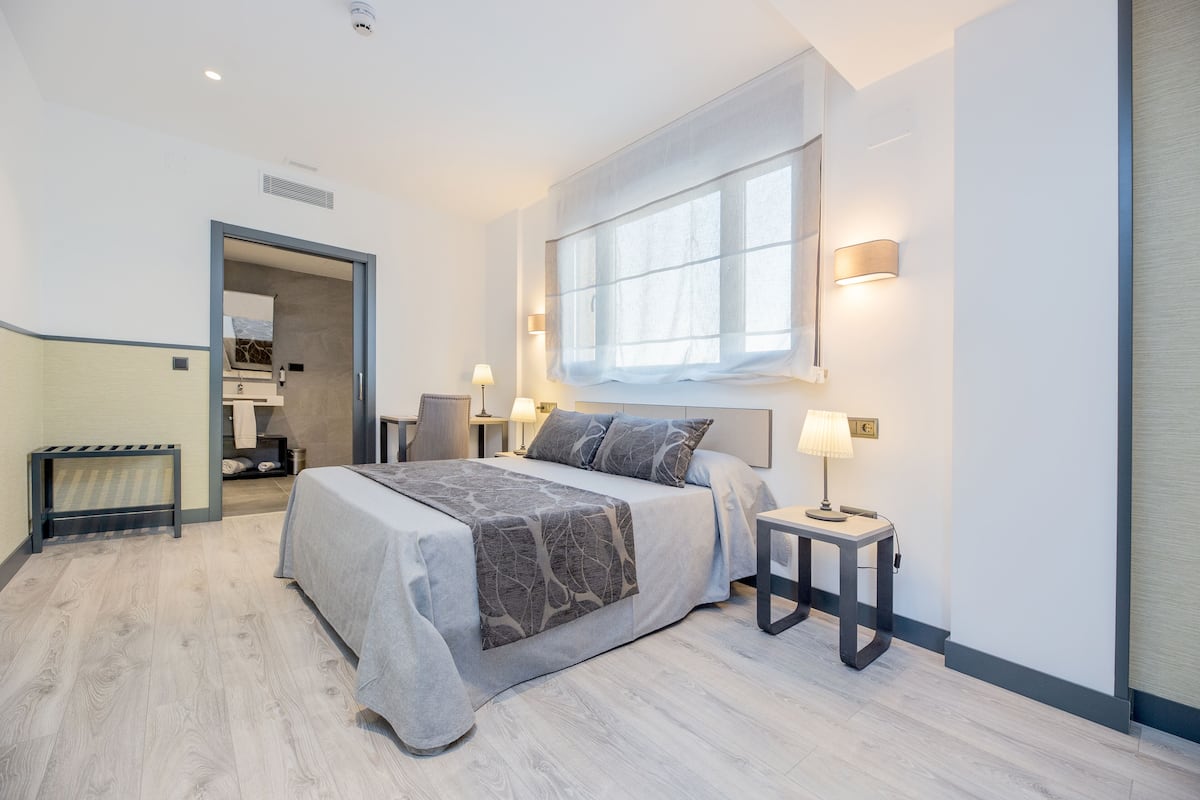A modern bedroom with a large bed, bedside lamps, and a window with curtains.