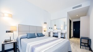 Una habitación de hotel moderna con una cama grande, mesitas de noche, un espejo y un baño con lavamanos y espejo.