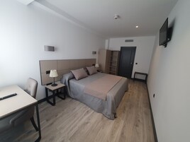 Una habitación de hotel moderna con una cama, mesitas de noche, un escritorio y un televisor montado en la pared.