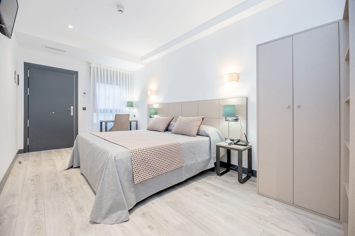A hotel room with a bed, bedside table, lamp, wardrobe, and a door.