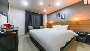 A hotel room with a large bed, a desk with a telephone, a chair, a desk lamp, and a nightstand with a lamp. - The Way Hotel (Changwon)