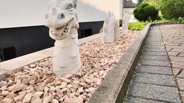 A pathway lined with white stone sculptures of animal heads, leading to a building with a white facade and dark base trim. - Nice apartment centrally located in the Rhine-Main area (Schöneck)