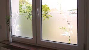 A window with frosted glass, a white vase with a plant, and a view of greenery outside. - Nice apartment centrally located in the Rhine-Main area (Schöneck)