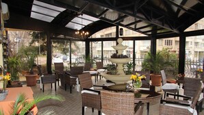 An indoor patio area with wicker furniture, a central fountain, and potted plants. - Charlino Plaza (Ruse)