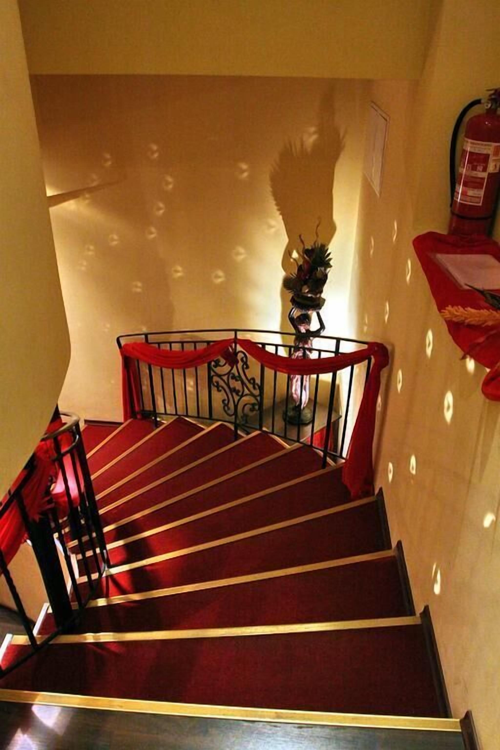 Un escalier avec des marches recouvertes de moquette rouge et des rampes noires, menant à l’étage supérieur.