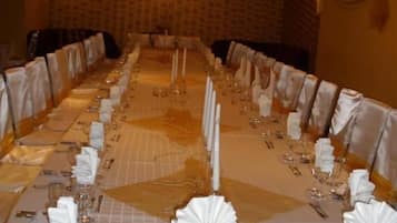 A long banquet table set for a formal event with white tablecloths, gold cutlery, and candle centerpieces.