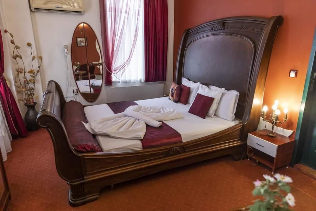 A large bed with a wooden headboard, a bedside table with a lamp, and a mirror on the wall.