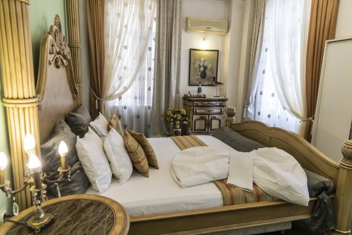 A neatly made bed with pillows and a blanket, a bedside table with a lamp, and a mirror.