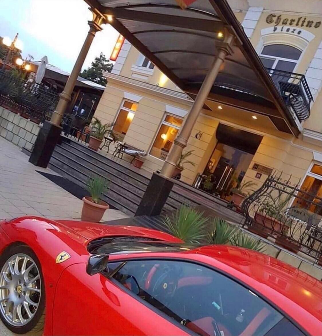 A red sports car parked in front of a building with a covered entrance and steps leading up to the entrance.