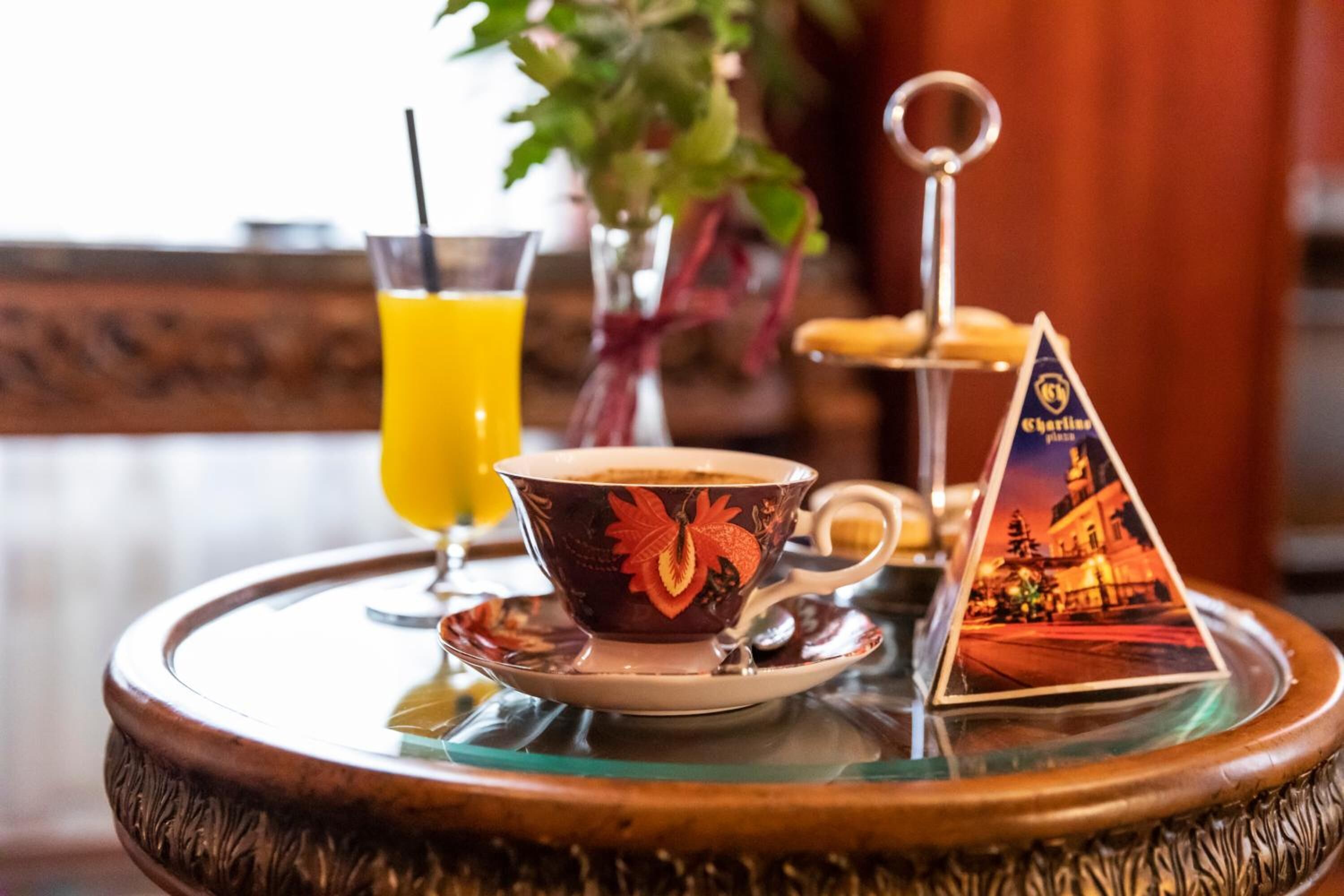 A table with a cup of coffee, a glass of orange juice, a small plant, and a decorative item.