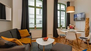Una sala de estar moderna con un sofá gris, una mesa de centro redonda y una zona de comedor con una mesa y sillas blancas.
