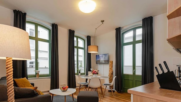 Una sala moderna con un sofá, una mesita redonda y un comedor con mesa y sillas. Hay una zona de cocina con mostrador y fregadero.