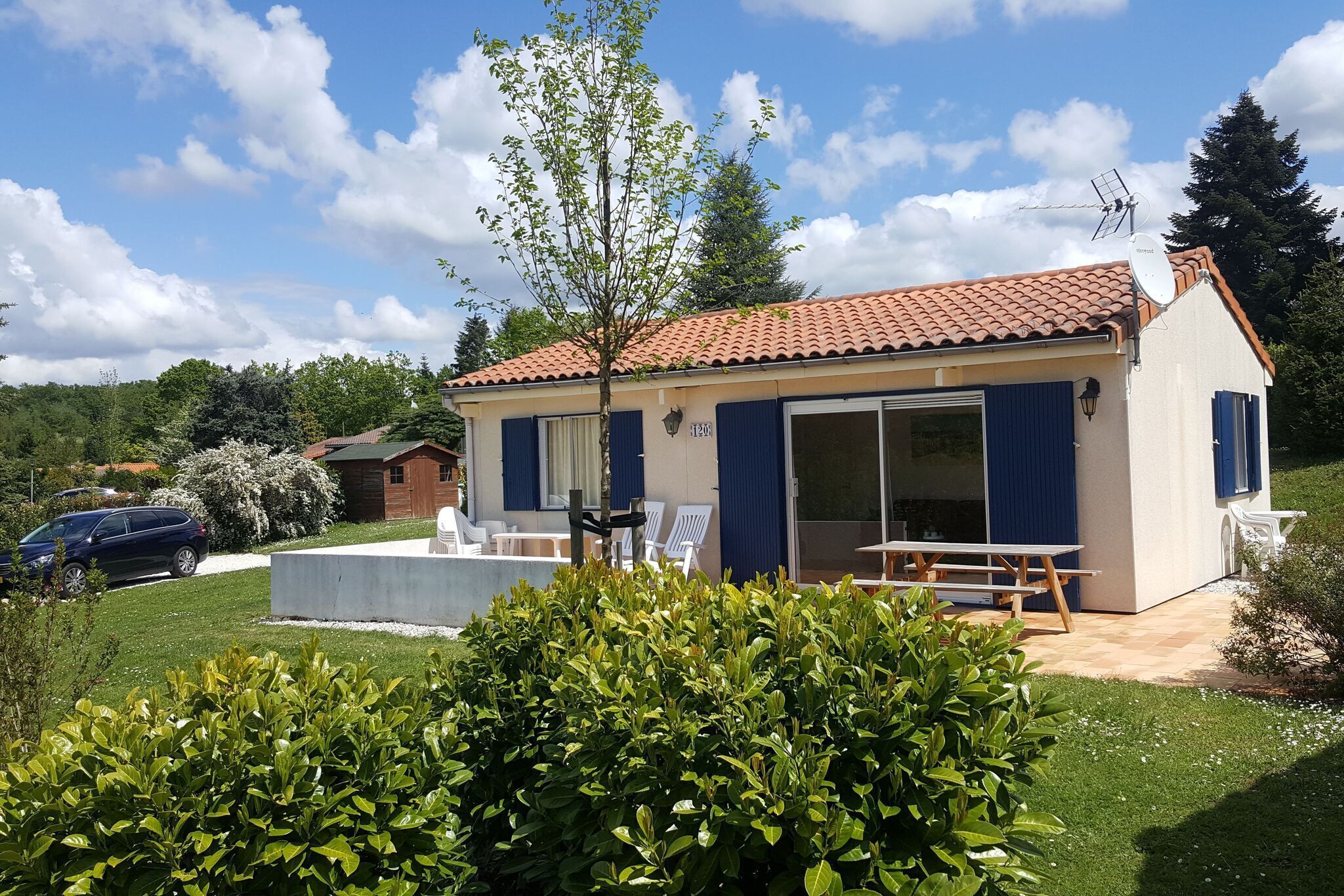 Een klein, gelijkvloers huis met een pannendak, een zwembad en een terras met tuinmeubilair.