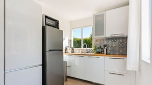 A modern kitchen with white cabinets, a stainless steel refrigerator, a wooden countertop, and a window with a view of greenery. - Urban Bungalow in Écuras with Swimming Pool (Écuras)