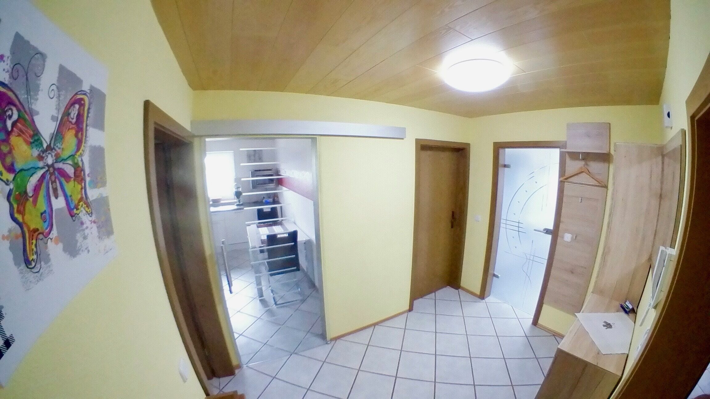 A hallway with a tiled floor, wooden doors, and a ceiling light.