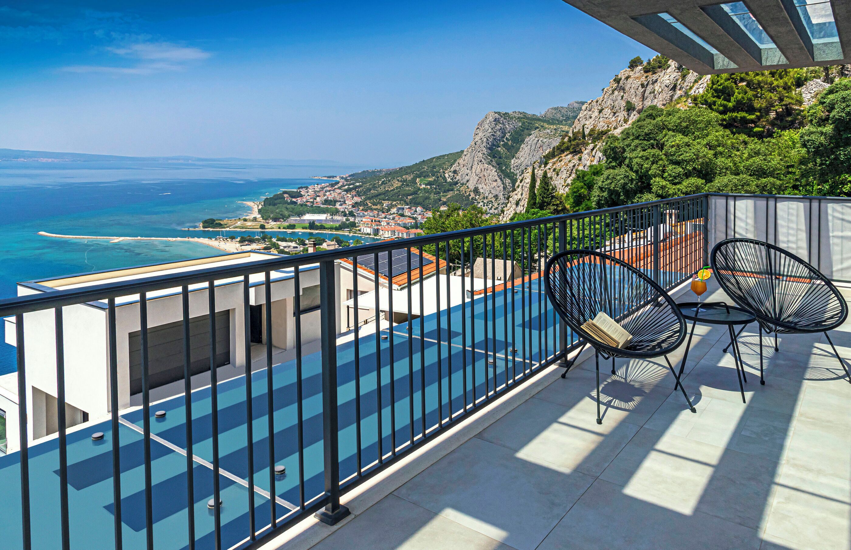 Ein Balkon mit Pool und Stühlen mit Blick auf eine Küstenstadt und Berge.