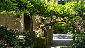 Een gebouw van steen met een klassiek ontwerp, inclusief een centraal bogenportaal en een kleine tuin met bloeiende planten.