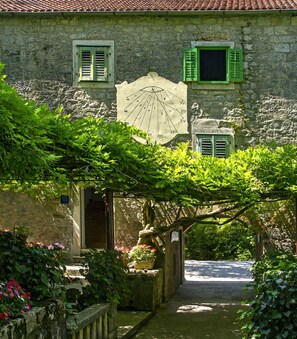 A stone building with a traditional design, featuring a central archway and a small garden area with flowering plants. - House Villa The View (Omis)