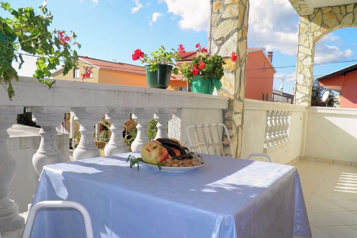 An outdoor dining area with a table set for two, surrounded by stone balustrades and potted plants.
