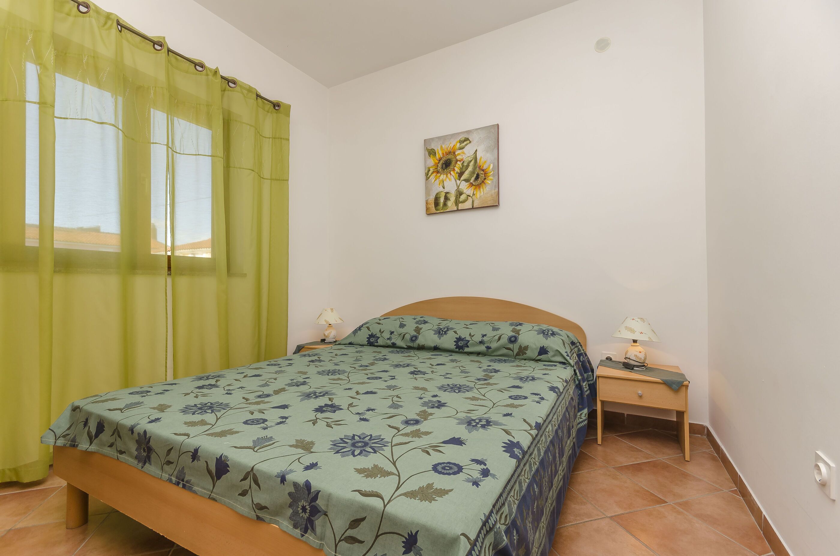 Un dormitorio con una cama, una mesita de noche, una lámpara y un cuadro en la pared.