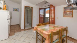 Un área de comedor con una mesa cubierta con un mantel floral, sillas de madera y un televisor montado en la pared.