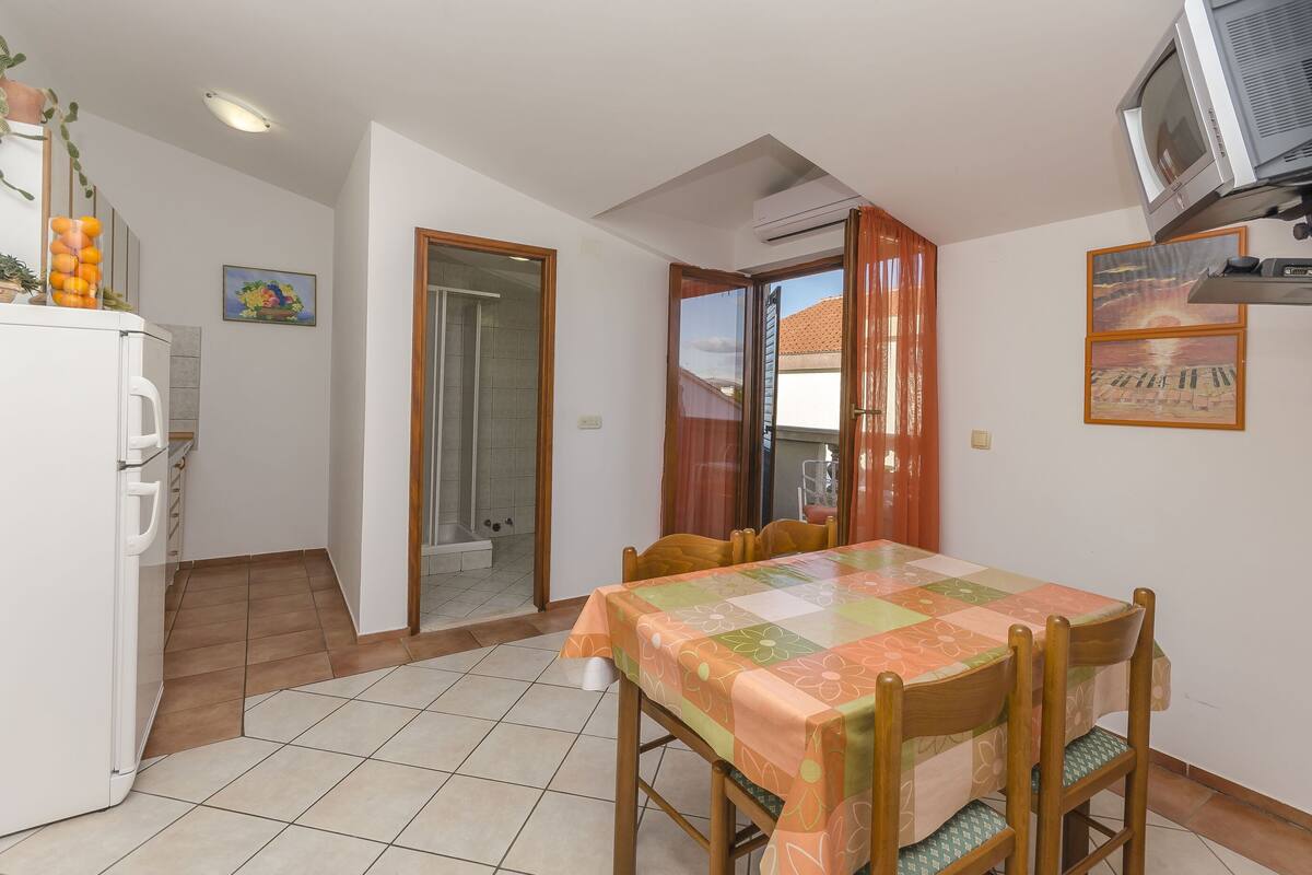 A dining area with a table covered in a floral tablecloth, wooden chairs, and a television mounted on the wall.