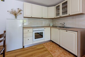 A kitchen with white cabinets, a built-in oven, a sink, and a chair.