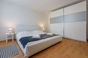 A bedroom with a bed, bedside tables, a nightstand, a wardrobe, and a patterned rug.