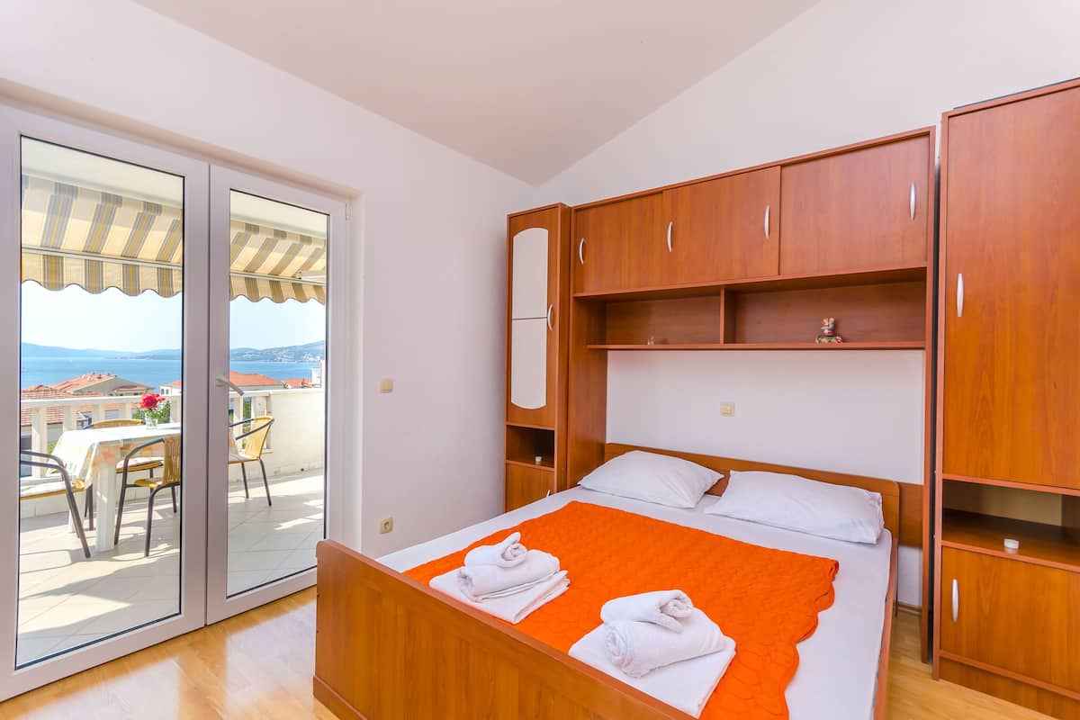 A bedroom with a bed, wooden wardrobe, and a balcony with a table and chairs.
