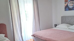 A bedroom with a bed, a nightstand, and a window with curtains. - Apartments Tily (Okrug Gornji)
