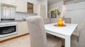 A modern kitchen with white cabinetry, a built-in oven, and a dining table with chairs. - Apartments Tily (Okrug Gornji)
